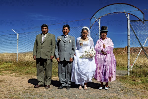 Wedding couple and companions in traditional clothes in front of fence and blue sky, traditional wedding in Bolivia