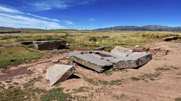Broken stone structures are spread across the vast countryside, under a clear sky, the archaeological site with the ruins of Tiwanaku in Bolivia