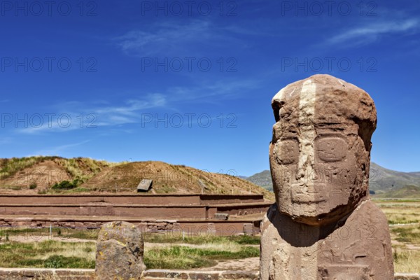 Stone statue in front of a ruined landscape under clear blue sky, The archaeological site with the ruins of Tiwanaku in Bolivia