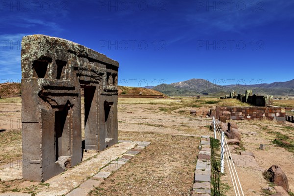 Ancient stone structures in a vast, mountainous landscape under clear blue skies, the archaeological site with the ruins of Tiwanaku in Bolivia