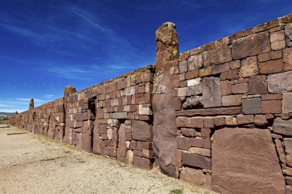Ancient stone wall stretching along a narrow path under blue sky, the archaeological site with the ruins of Tiwanaku in Bolivia