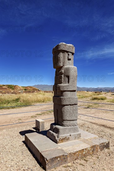 Ancient stone figure standing upright on a platform against a clear sky, the archaeological site with the ruins of Tiwanaku in Bolivia