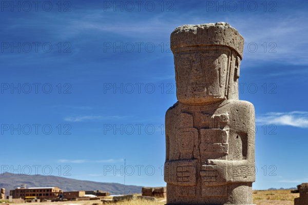 Large ancient stone statue under clear sky, showing detailed engravings, the archaeological site with the ruins of Tiwanaku in Bolivia