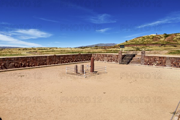 A rectangular square with stone pillars surrounded by ruins under a clear sky, The archaeological site with the ruins of Tiwanaku in Bolivia