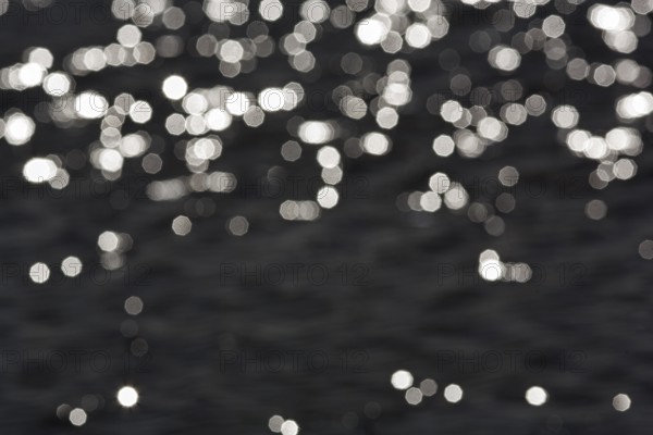 Abstract black background, sparkling white lights, bokeh balls, light reflections on water surface, octagonal light spots, copy space, background image, Sicily, southern Italy, Italy