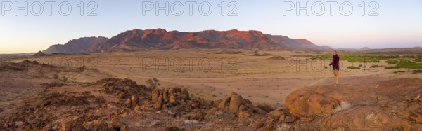 Young woman standing in desert landscape with Brandberg in morning light, at sunrise, Erongo, Damaraland, Namibia
