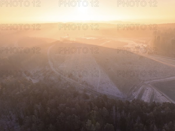 A large hill surrounded by forest, in foggy sunrise, old deposit, construction site for PV open space plant, Lindenrain, Calw, Germany