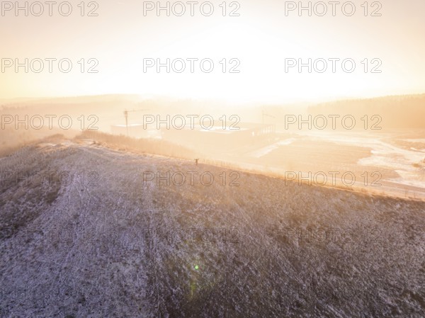 Snow-covered hill in warm sunrise atmosphere, old deposit, construction site for PV open space plant, Lindenrain, Calw, Germany