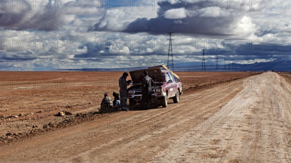 A car is being repaired on the side of the road by several people in the desert, The landscape of the Altiplanos near Uyuni in Bolivia