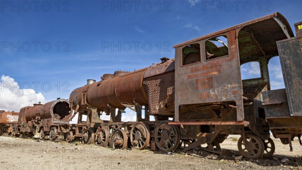 Long line of rusty locomotives in an open desert landscape under clear skies, old rusty locomotives at the train cemetery near Uyuni in the Altiplano in Bolivia