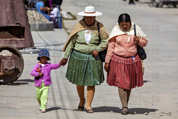 Two woman and a child in colorful, traditional clothing walking hand in hand on the street, people in an altiplano near Uyuni in Bolivia