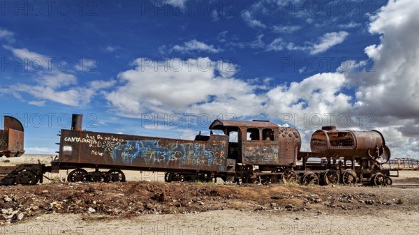 Weathered locomotive in the desert with clouds in the blue sky, old rusty locomotives at the train cemetery near Uyuni in the Altiplano in Bolivia