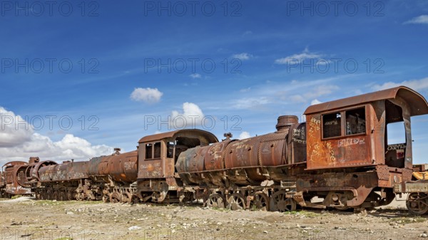 Rusty old trains on dry ground under blue skies, old rusty locomotives at the train cemetery near Uyuni in the Altiplano in Bolivia