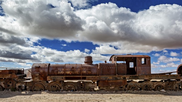 Rusty locomotive in a barren desert landscape with dramatic clouds, old rusty locomotives at the train cemetery near Uyuni in the Altiplano in Bolivia