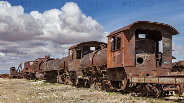 Several rusted locomotives on a dry surface under a cloudy sky, old rusty locomotives at the train cemetery near Uyuni in the Altiplano in Bolivia