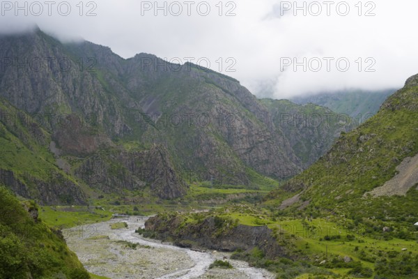 Mighty mountains with cloud cover, a river cuts through the green valley with rocks and vegetation, Tergi River, Terek, Darial Gorge, Dariel Gorge, Kazbegi, Stepansminda, Georgian Military Highway, Mtskheta-Mtianeti Province, High Caucasus, Georgia