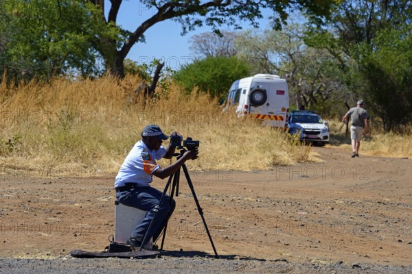 A policeman controls traffic with a camera on a tripod on the side of the road, man must pay fine for driving at excessive speed, Botswana