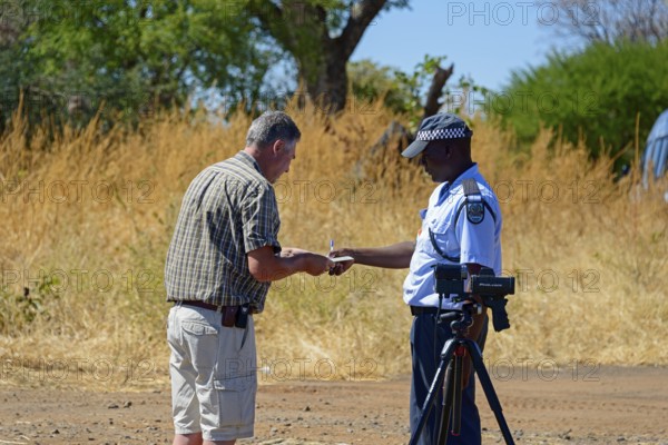 A police officer talks to a man on the side of the road in a rural setting, man must pay fine for driving at excessive speed, Botswana