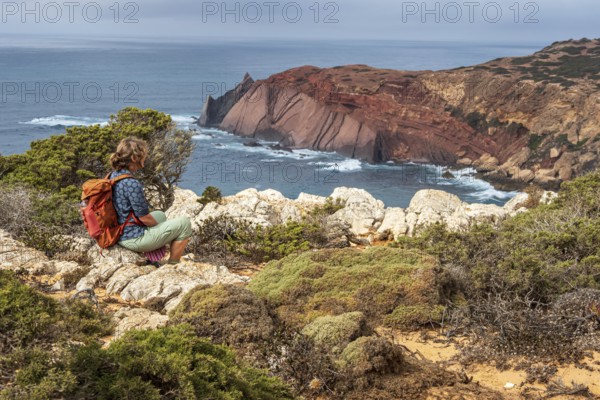 Hiking woman takes a break, view over cliff, Fishermens Trail, Rosa Vicentina, western Algarve just north of cape Cabo de Sao Vicente, Portugal