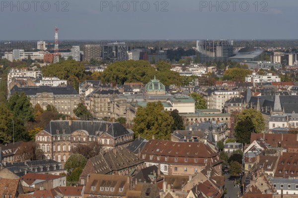 The stone balcony offers a view of the city of Strasbourg. Houses and buildings can be seen under a cloudy sky. Architectural details surround the balcony. Bas Rhin, Alsace, France