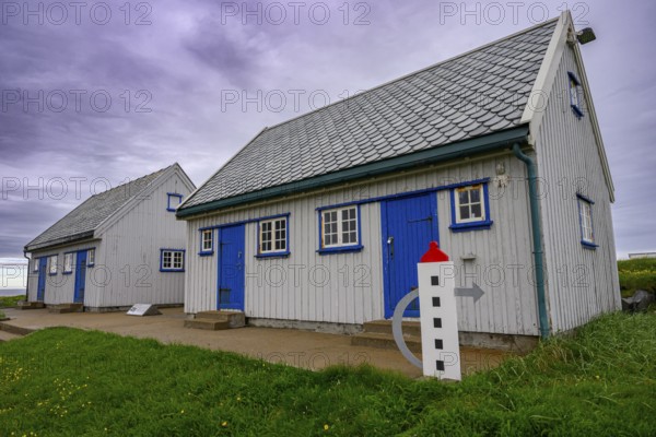 An old grey lighthouse dictionary house with a sloping roof at Kjølnes Fyr, small windows and railings in a rural area, Berlevåg, Finnmark, Norway