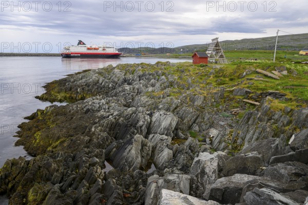 The Hurtigrouten Hurtigruten ship Kong Harald arrives at Berlevag harbour, on the horizon with a cloudy sky, Berlevåg, Finnmark, Norway