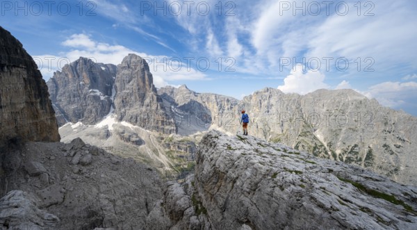 Mountaineers on a rock in front of picturesque mountain landscape with rocky peaks, Via Ferrata SOSAT via ferrata, summit of Cima Tosa in the back, Brenta Mountains, Trentino, Italy