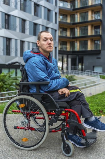 Young adult man with a disability sitting in a wheelchair while looking forward, portraying concepts of mobility, independence, and inclusive urban lifestyle outside a modern building