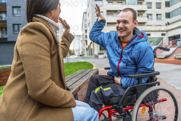 Joyful disabled man in a red wheelchair sharing a high five with a woman on a bench, symbolizing inclusion, friendship, and support in an urban setting