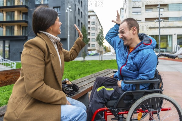 Young woman on a bench in the city happily high fiving a smiling man in a wheelchair, illustrating friendship, support, and inclusion in an urban setting