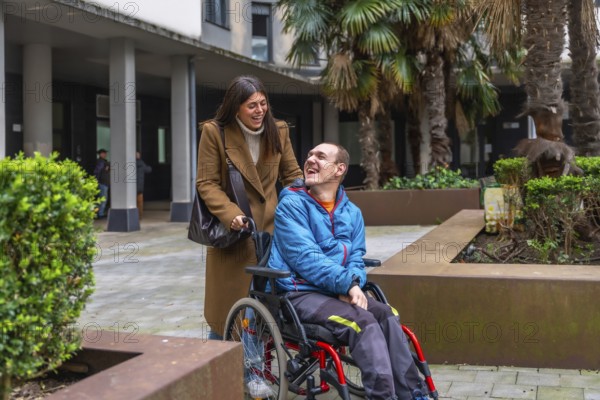 Smiling caregiver pushing wheelchair, sharing warm conversation and laughter with happy man outdoors, promoting inclusion, companionship and active assisted living in urban setting