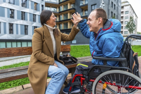 Woman and disabled man in wheelchair laughing, high fiving, and sharing a happy moment during an outdoor session, symbolizing support, friendship, and positive connection