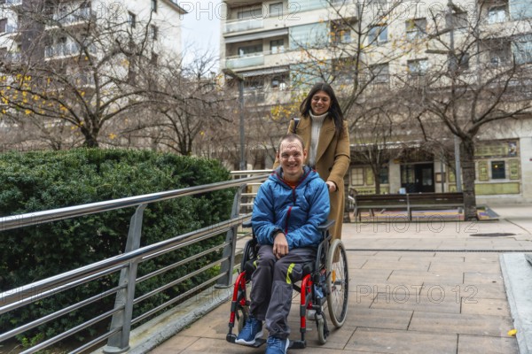 Happy woman caregiver assisting a young man with a disability, pushing him in his wheelchair along an accessible urban ramp, promoting inclusion and support