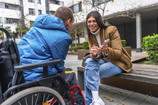Woman and man with disability in wheelchair engaging in an inclusive outdoor conversation, sharing supportive interaction while the woman uses a mobile phone