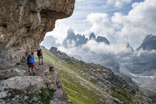 Two mountaineers on a path in front of a picturesque mountain landscape with rocky peaks, Via Ferrata SOSAT via ferrata, Cima Tosa summit in the back, Brenta Mountains, Trentino, Italy