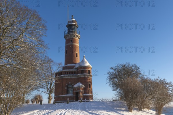Holtenau lighthouse at the entrance of the Kiel Canal in winter, west bank of the Kiel Fjord, shipping, brick building from 1895, round tower, orientation, sea sign, beacon, ground floor with wedding room, trees, snow, blue sky, Baltic Sea, Kiel, Germany