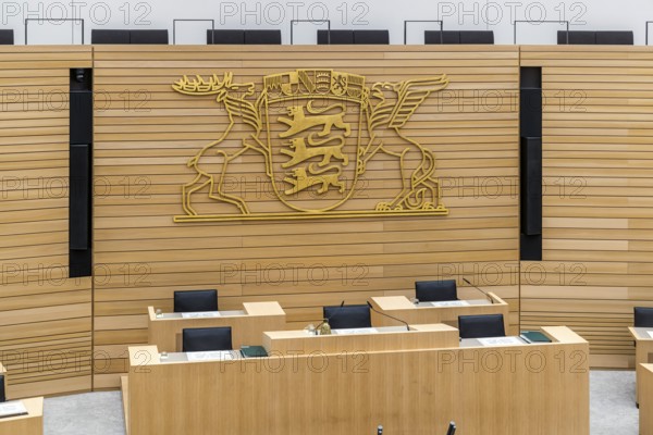 Plenary hall deserted with the seats of deputies and the government bank. Behind it is the coat of arms of the federal state. The state parliament of Baden-Württemberg is the state parliament based in Stuttgart, Baden-Württemberg, Germany