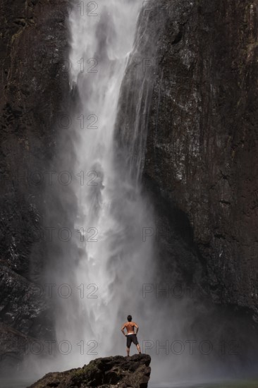Daytime scene at Wallaman Falls with a fit man in swim trunks below the waterfall, Queensland, Australia