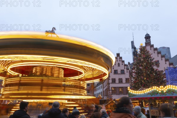 December 22, 2025, Frankfurt Christmas Market on Roemerberg with the skyline in the background at twilight. Lights are shining and a children's carousel is spinning, Frankfurt, Hesse, Germany