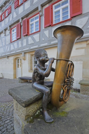 Sculpture boy with tuba by Guido Messer 1991, modern art, bronze sculpture, playing music, tuba, brass instrument, sitting, jack, size comparison, big, small, big cheeks, blowing, half-timbered house, music school, Waldenbuch, Baden-Württemberg, Germany