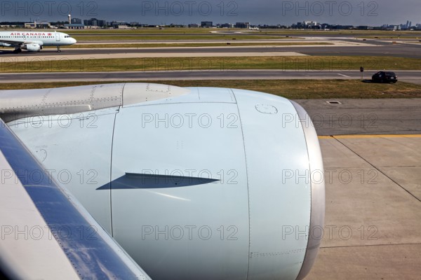 Aircraft turbine near the runway with a passing car and another aircraft in the background, view from an airplane of Toronto airport in Canada