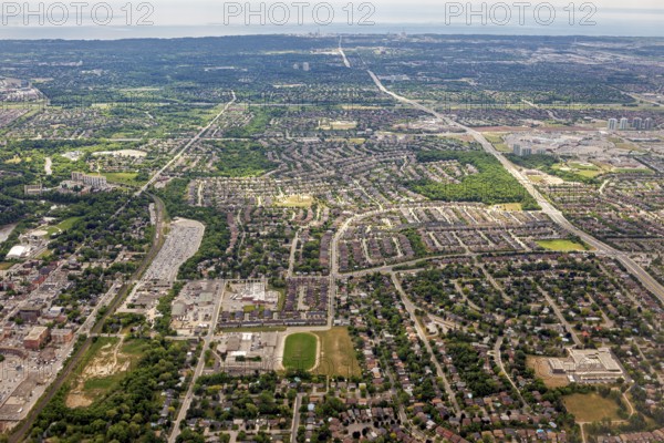 Densely populated residential areas and green spaces stretch out under a cloudy sky seen from the air, view from an airplane of the suburbs of Toronto in Canada