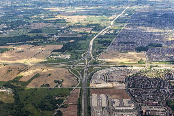 An aerial view shows a vast landscape of highways, fields and densely built suburbs under clouds, seen from an airplane of the suburbs of Toronto in Canada