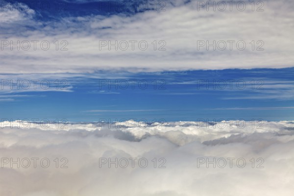 Wide view of white clouds under bright blue sky, on an airplane above the clouds