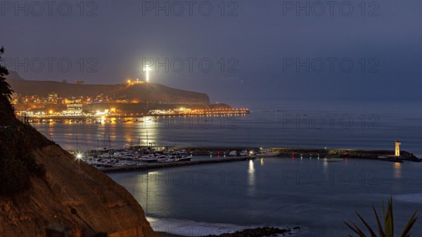 Coastal landscape at night with illuminated cross on a hill and harbor lights, calm sea atmosphere, at night on the coast in Lima in Peru