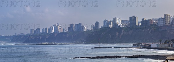 View of a coastal town with skyscrapers on cliffs and waves under a blue sky, The coast with the skyline of Lima in Peru