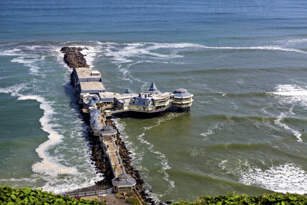 Pier with a building in the middle of the sea, surrounded by waves and under a blue sky, a seaside resort with restaurant on the coast near Lima in Peru