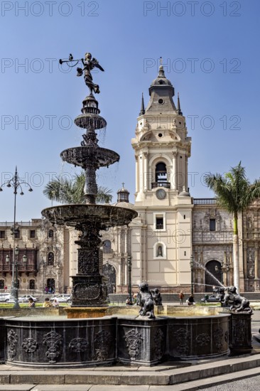 Decorative fountain with sculptures in an urban square surrounded by palm trees and a tower, Downtown Lima in Peru