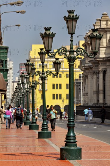 Row of green street lights along a busy walkway with architectural buildings in the background, Downtown Lima in Peru