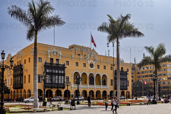 Colonial building with arches and national flag, surrounded by palm trees, in a sunny square, The historic center of Lima in Peru